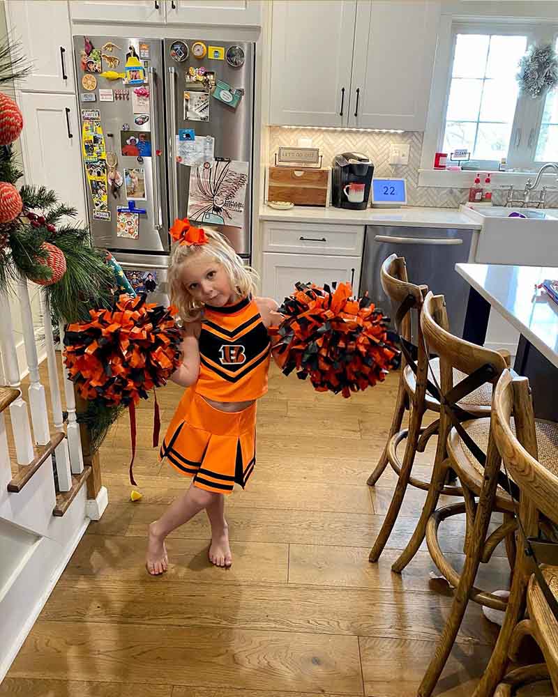 Blair - Little Girl in Cheerleading Outfit with Pom Poms While Standing in the Kitchen of Their House