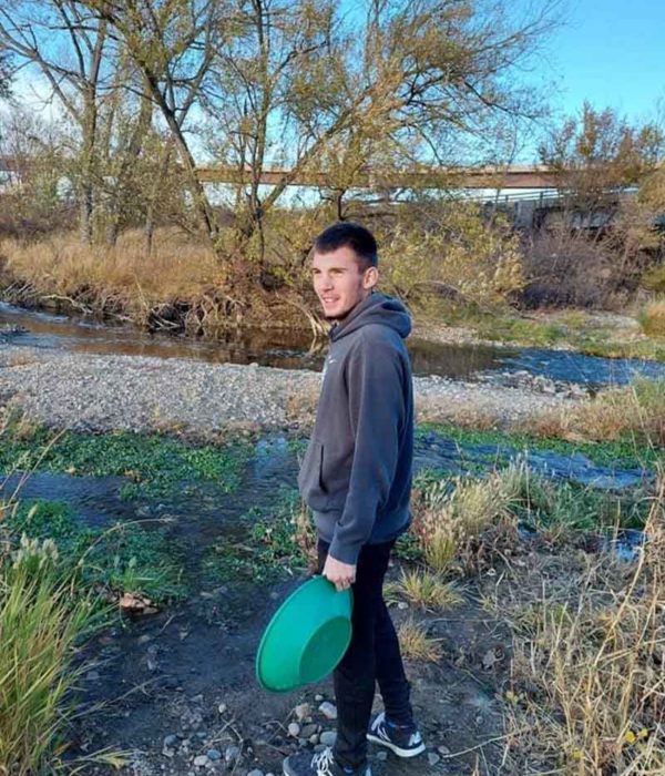 Susan - Man Smiling Outside While Holding a Green Bucket in Front of a River