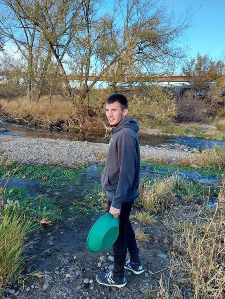 Susan - Man Smiling Outside While Holding a Green Bucket in Front of a River